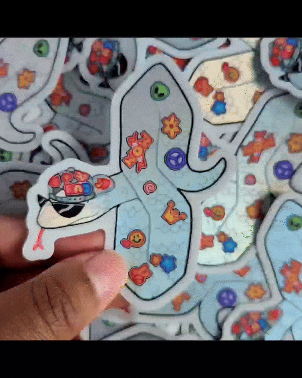 A holographic snake sticker in the shape of the ubiquitous "cool S" wearing a backwards cap and decorated in small stickers. The snake is wearing sunglasses.